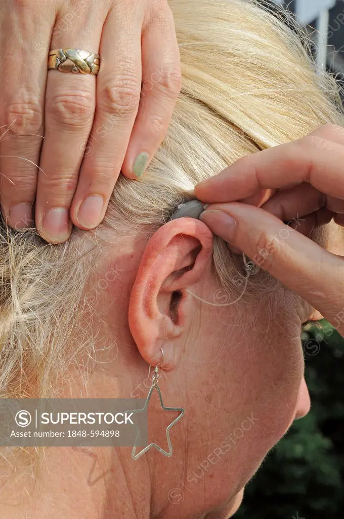 Modern small hearing aid behind the ear of a woman, 55 - 60 years, hardness of hearing