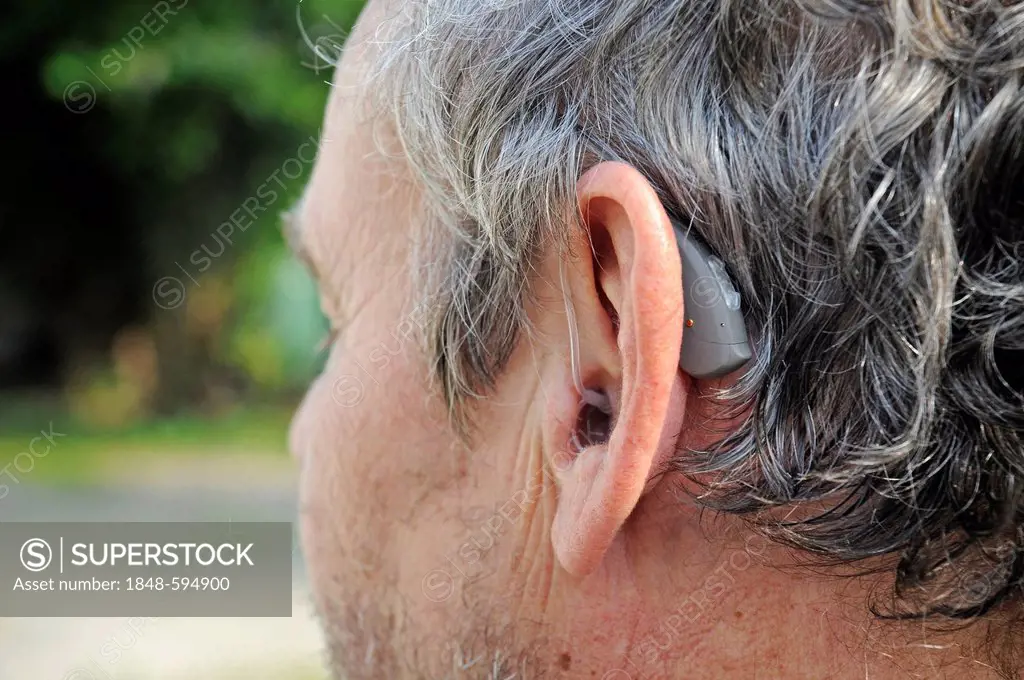 Hearing aid behind the ear of a man, 65 - 70 years, hardness of hearing