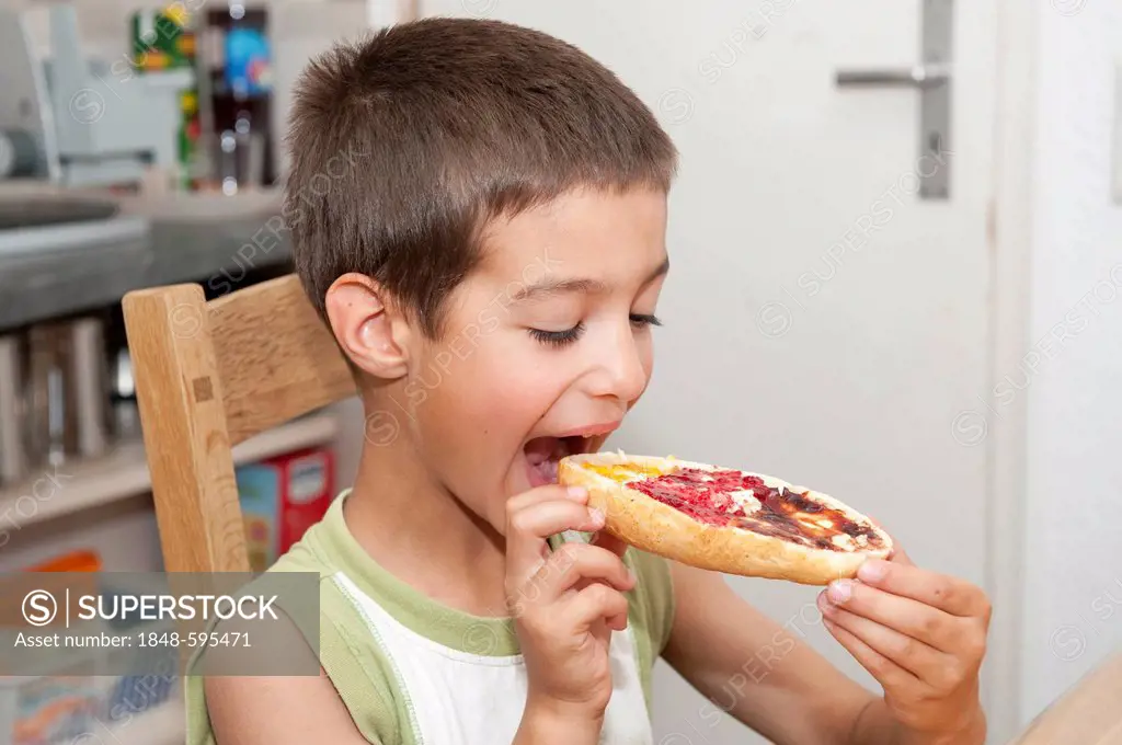 Boy, 7 years, biting into a bun with various jams