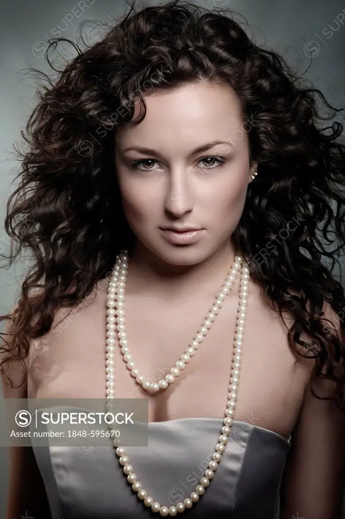 Young woman with curly brown hair and pearl necklace, beauty portrait