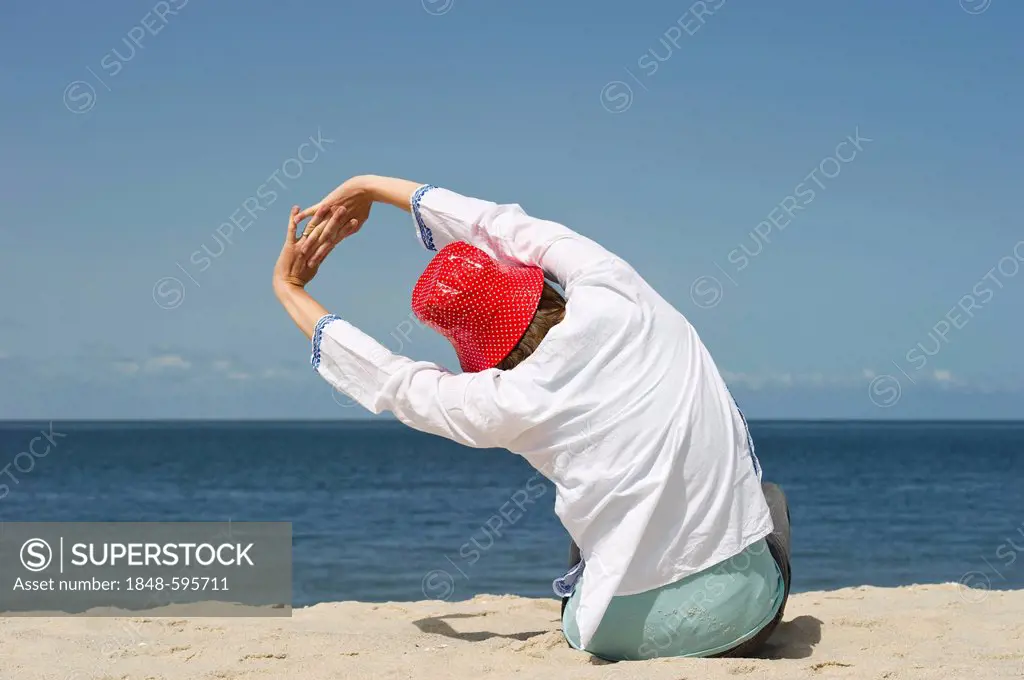 Woman wearing a red hat relaxing and stretching on the beach, Sylt island, Schleswig-Holstein, Germany, Europe