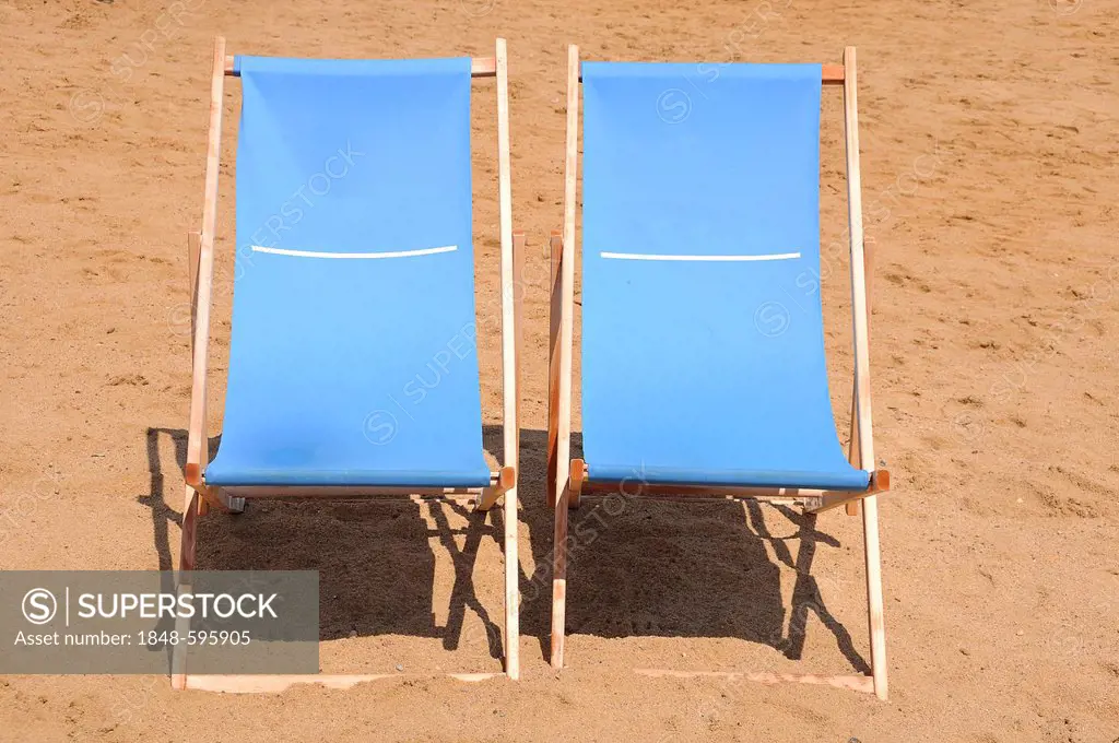 Two blue wooden deckchairs on the beach