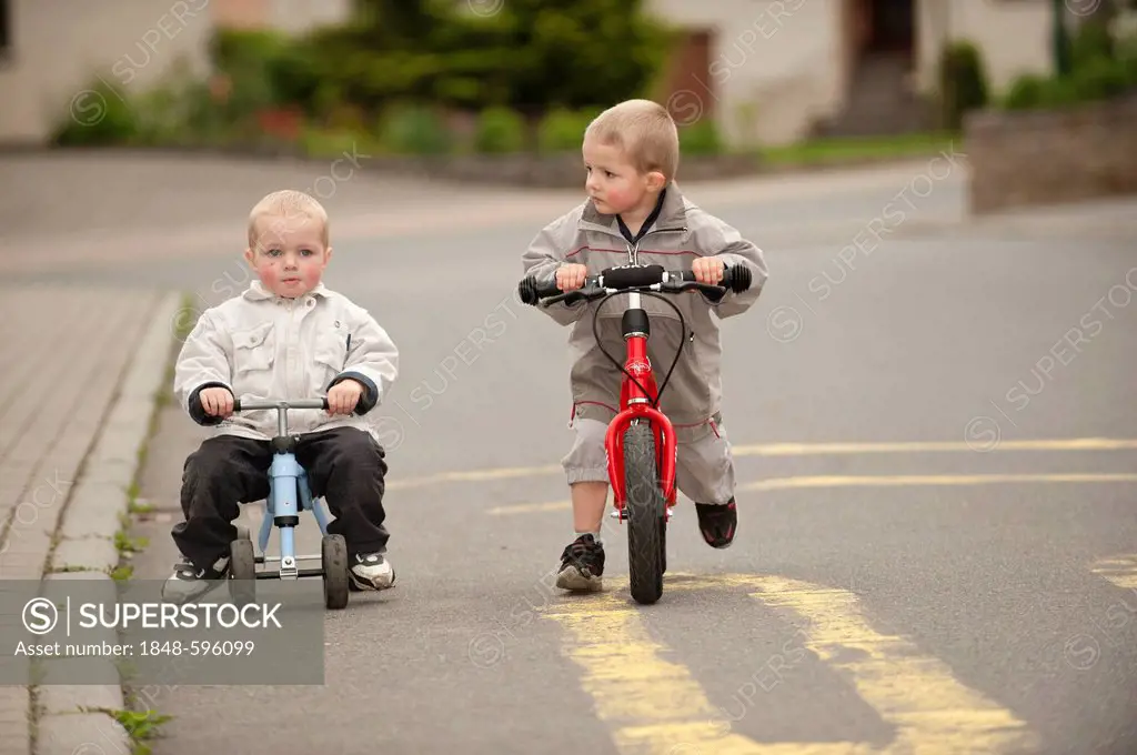 Two boys, 4 and 3 years, riding balance bicycle and Pukybike on the road