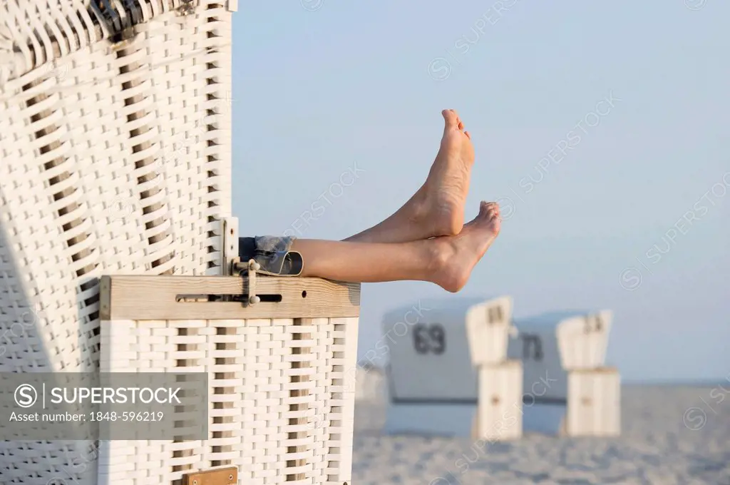 Feet protruding from a white roofed wicker beach chair on Westerland beach, Sylt island, Schleswig-Holstein, Germany, Europe