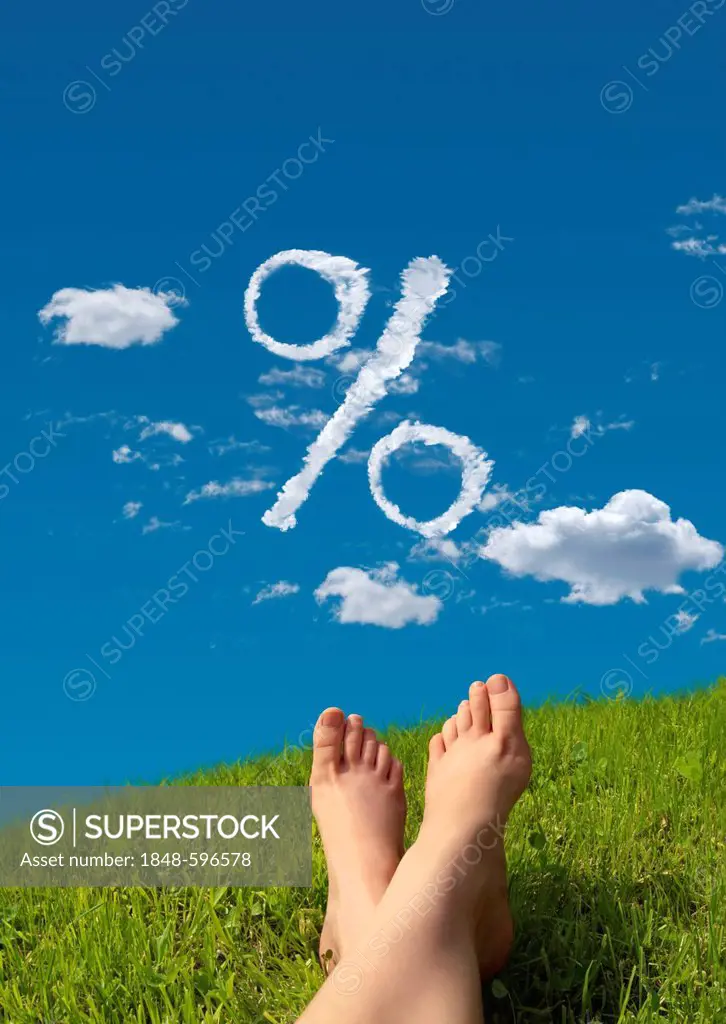 Woman lying on a meadow, detail of feet with a cloud formation shaped like a percent symbol in the sky