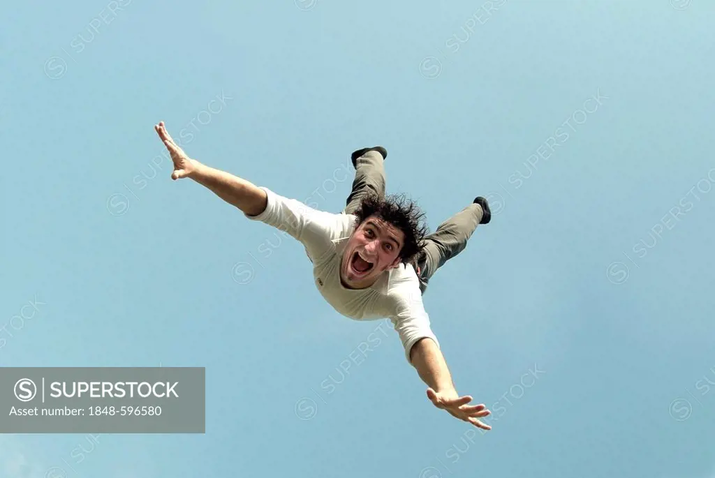 Young man flying with outstretched arms, seen from below