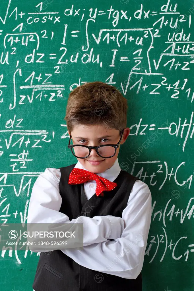 Schoolboy wearing glasses and a bow tie in front of a blackboard with math equations
