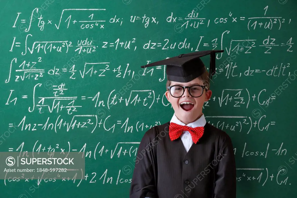 Schoolboy wearing a graduation cap, glasses and a bow tie in front of a blackboard with math equations