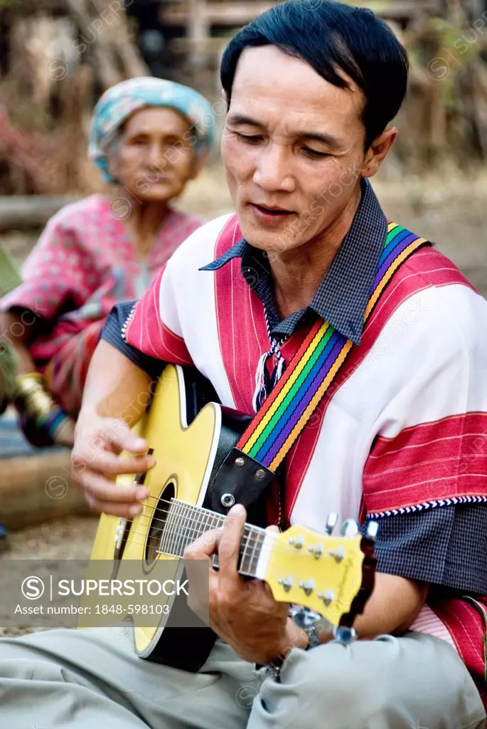 Traditionally dressed Karen hill tribe man playing guitar in Mae Lai village, Thailand, Asia