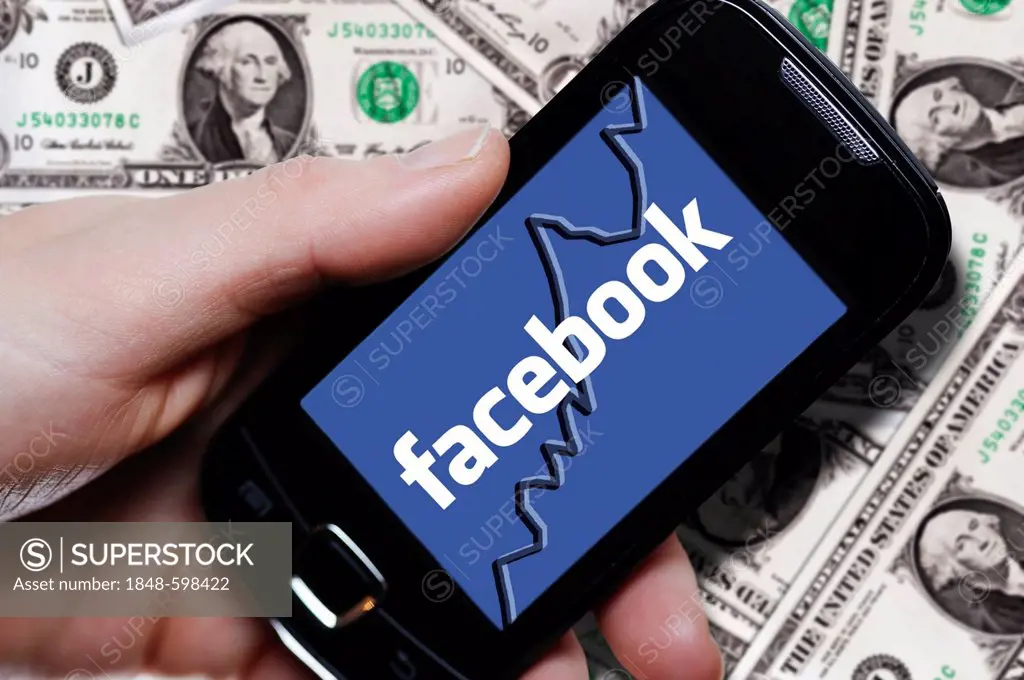 Hand holding a smartphone with a Facebook logo in front of dollar bills, symbolic image for the Facebook IPO