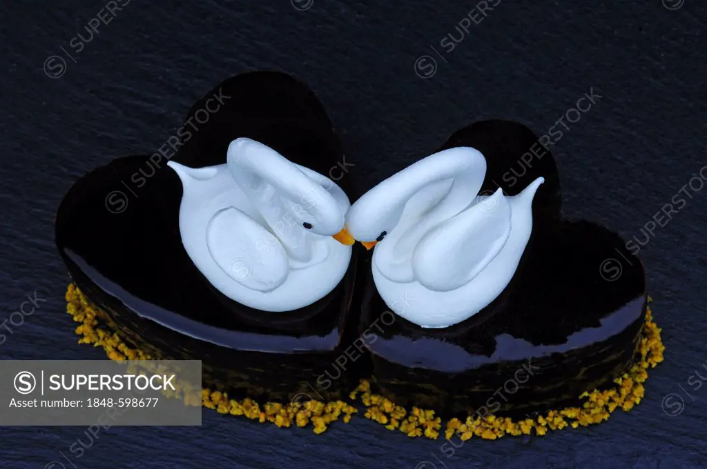 Two meringue swans on a chocolate heart, beaks made from apricots, on a slate in a patisserie