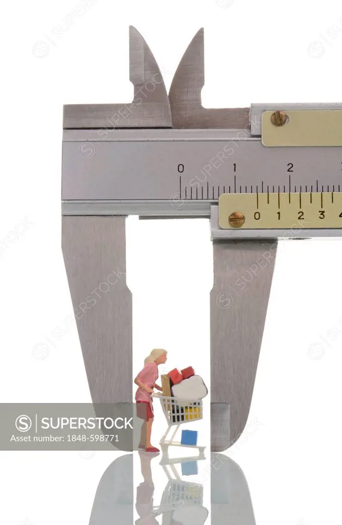 Female miniature figure with an overfull shopping cart in a caliper gauge, symbolic image for shopping fever