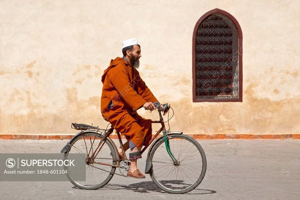 Cyclist wearing a Djellaba, a traditional robe, cycling in front of the Ben Youssef Madrasa in the Medina, historic district, UNESCO World Heritage si...