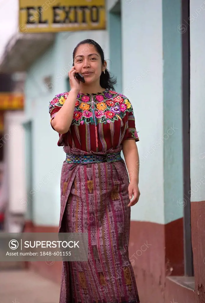 A native Kakchiquel wearing traditional dress, Huipil, walks while talking on her cell phone, Patzún, Chimaltenango Department, Guatemala, Central Ame...