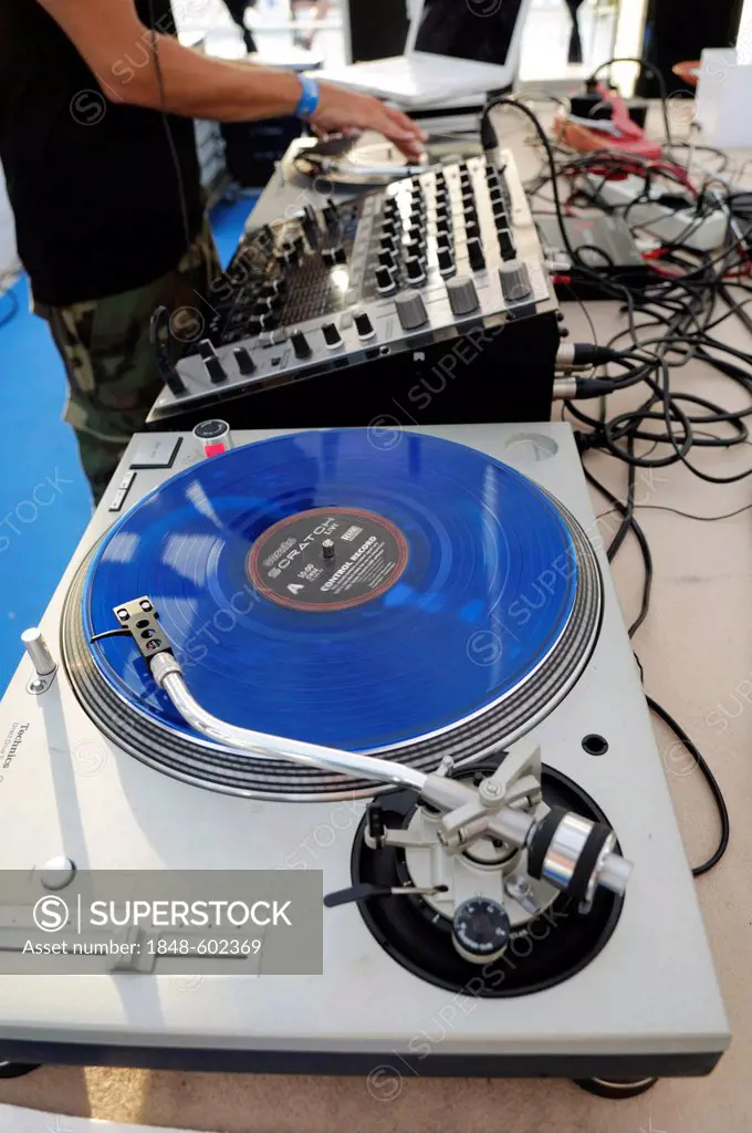 DJ turning knobs on a mixing console, in the foreground is a blue scratch disc on a turntable during the Electrobeach Festival at Benidorm, Spain, Eur...