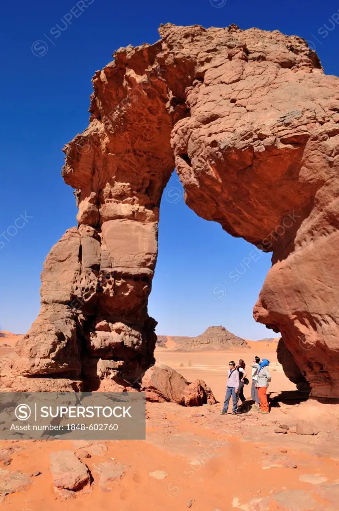Tourists below the rock arch or natural bridge of In Tehak, Acacus Mountains or Tadrart Acacus range, Tassili n'Ajjer National Park, Unesco World Heri...