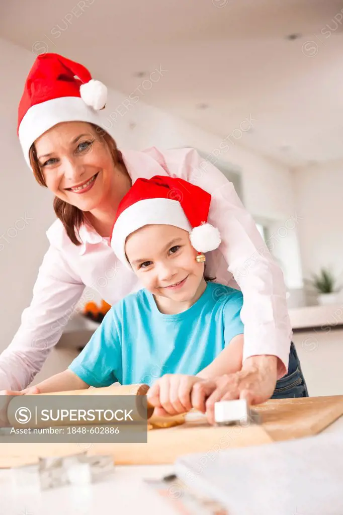 Girl and her mother baking Christmas cookies while wearing Santa Claus hats