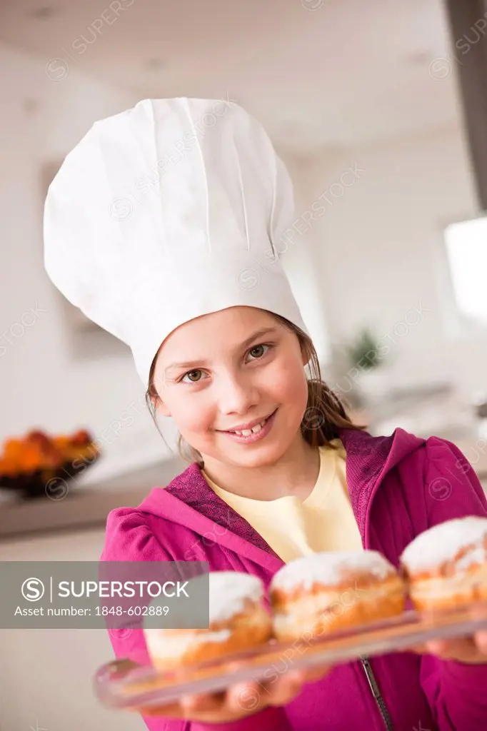 Girl in a chef's hat presenting a Berliner or filled doughnut