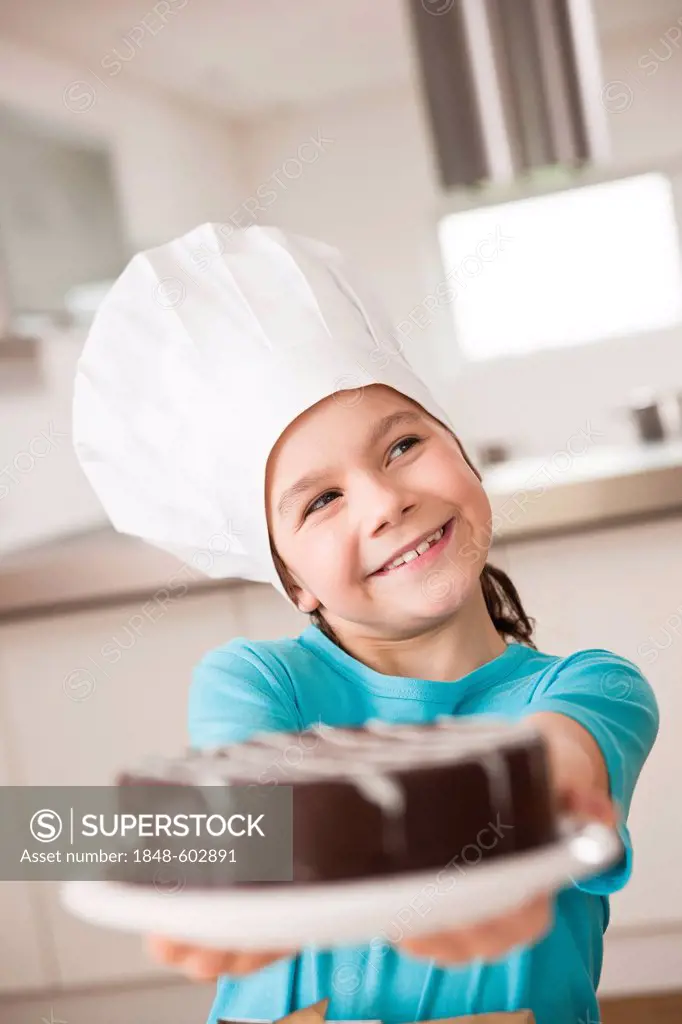 Girl in a chef's hat presenting a chocolate cake