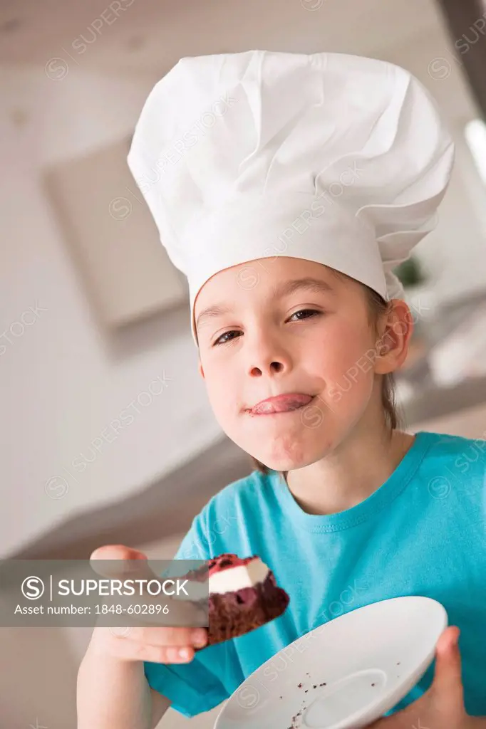 Little girl with chef's hat eating a piece of cake