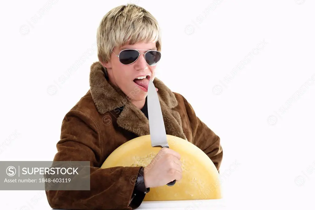 Young man with half a wheel of cheese and a knife at his outstretched tongue