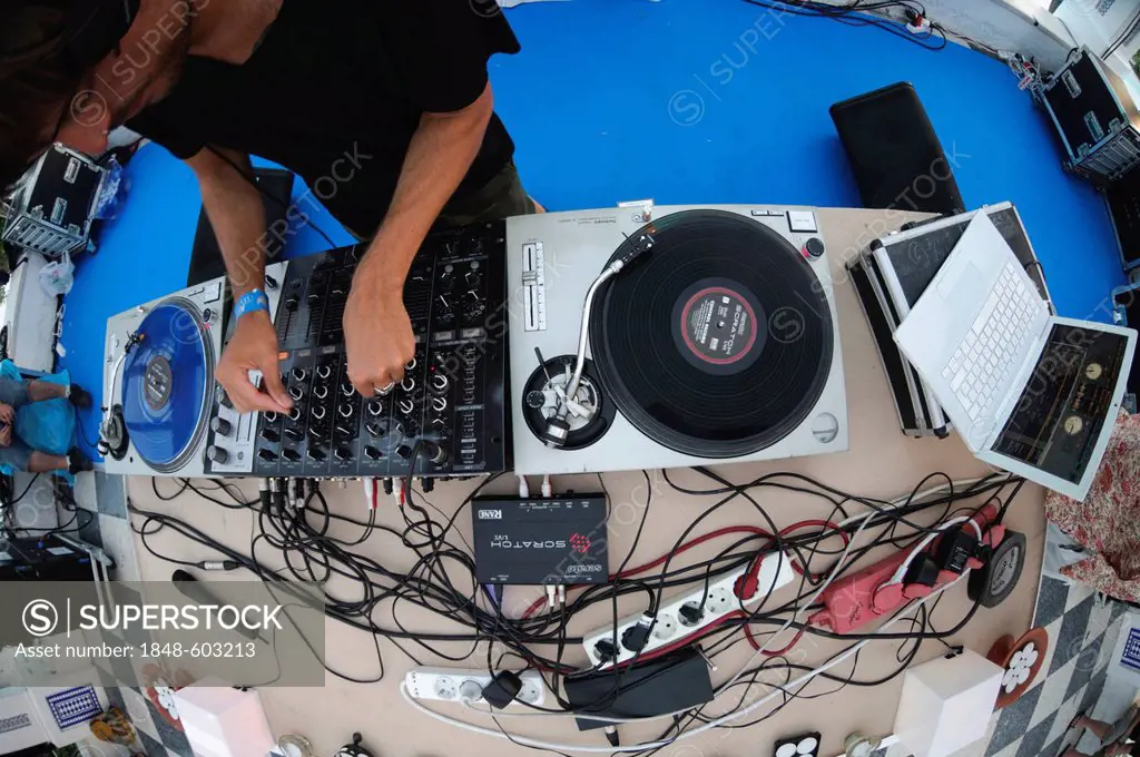 DJ turning knobs on a mixing console between turntables with blue and black scratch discs during the Electrobeach Festival at Benidorm, Spain, Europe