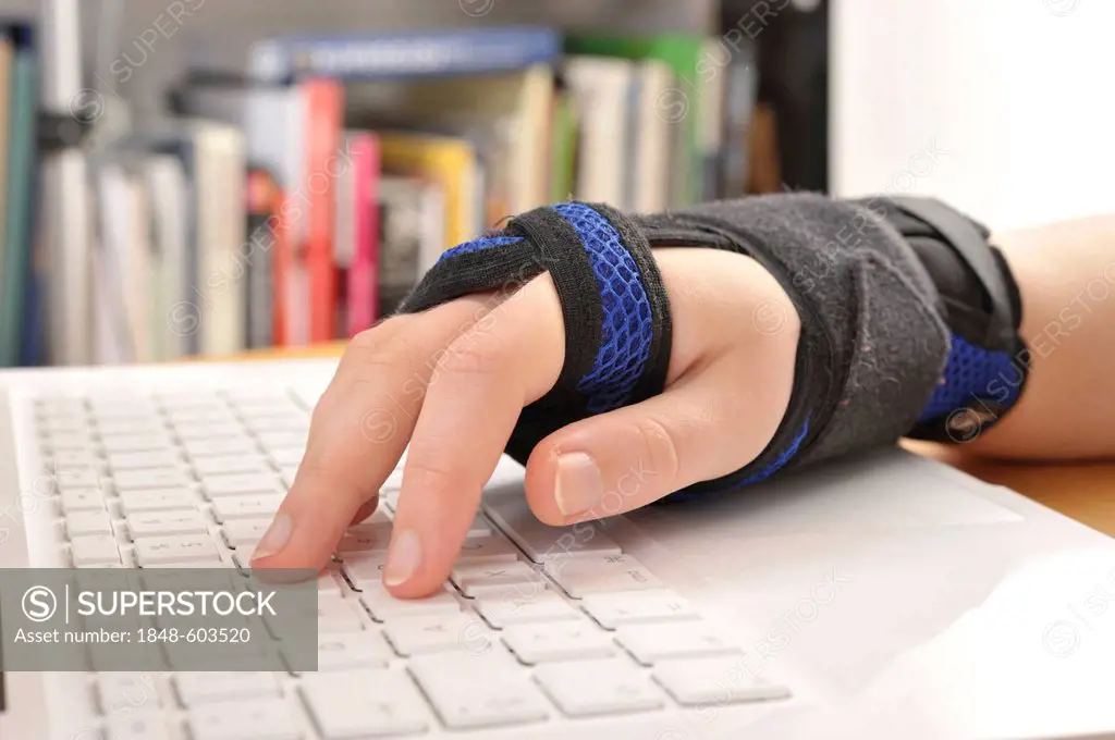 Hand wearing a support bandage using a computer keyboard