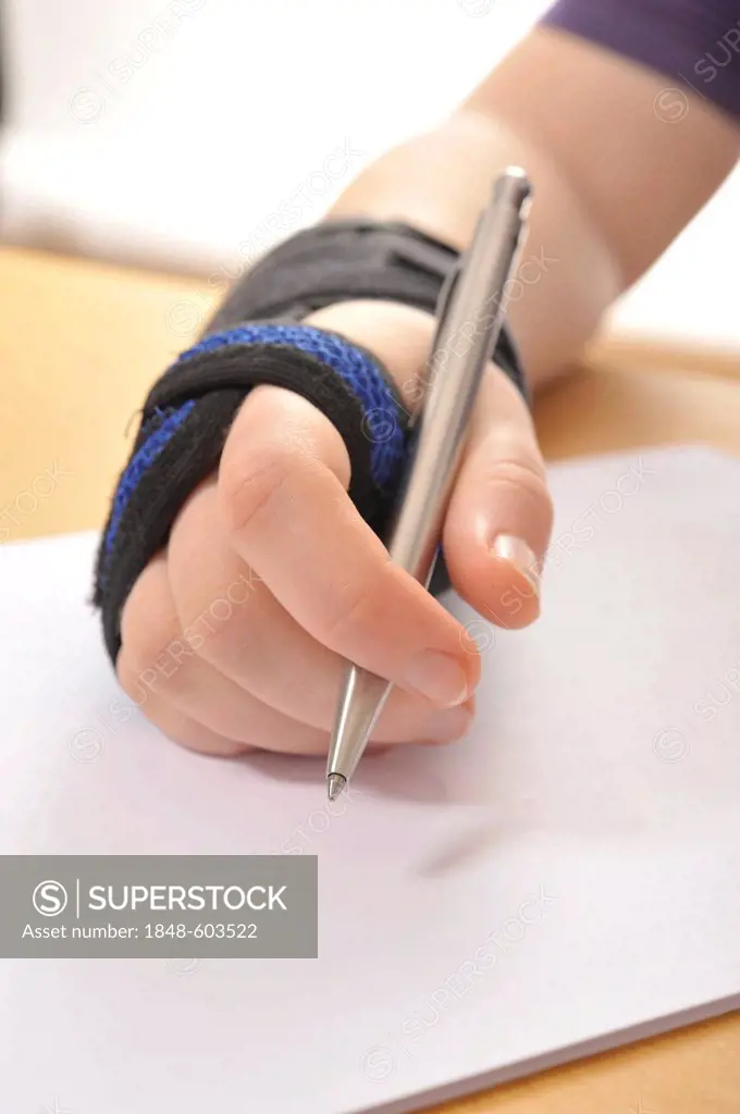 Hand wearing a support bandage holding a pen