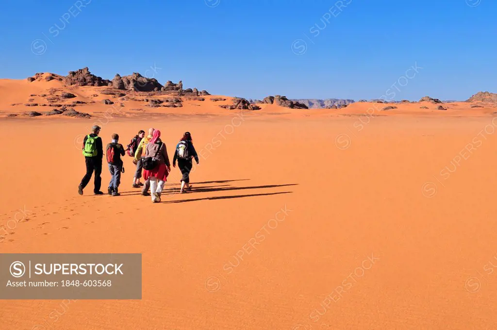Group of tourists hiking in the dunes of Tin Merzouga, Acacus Mountains or Tadrart Acacus range, Tassili n'Ajjer National Park, Unesco World Heritage ...