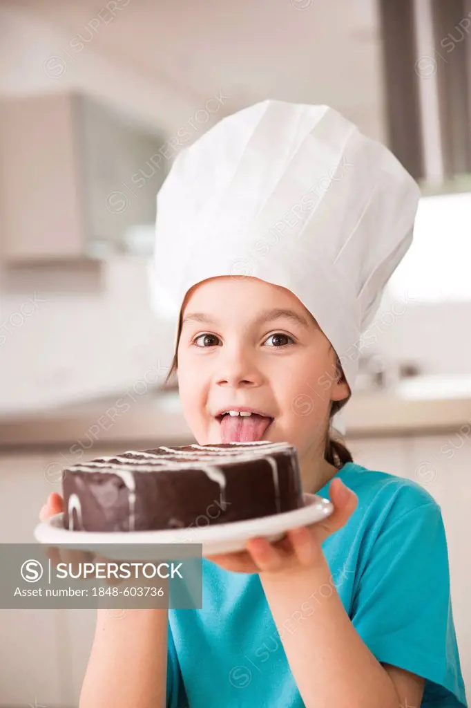 Little girl with chef hatt licks a chocolate cake
