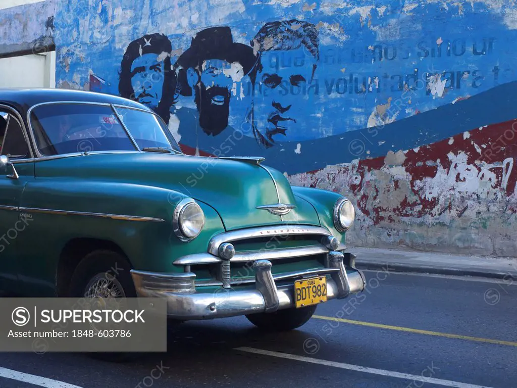 American vintage cars as a Cuban taxi driving along a wall with paintings of Fidel Castro and Che Guevara, Havana, Cuba, Latin America