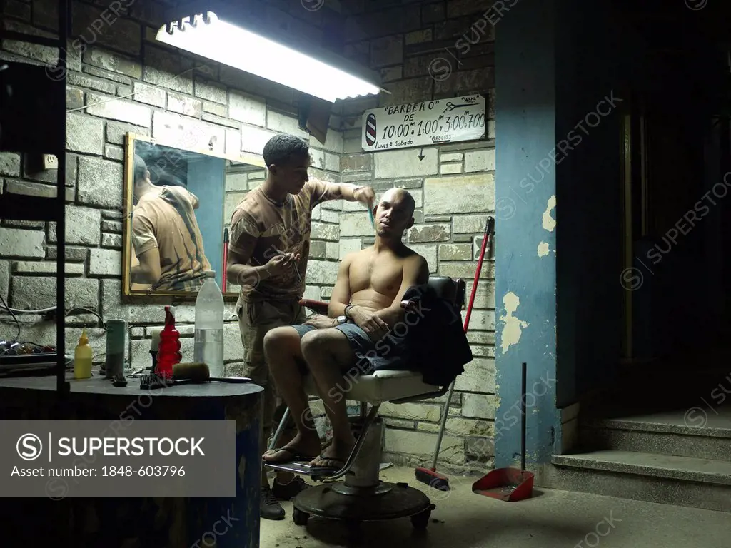 Barber cutting the hair of a Cubans man under fluorescent light in the hair salon at night, Havana, Cuba, Latin America