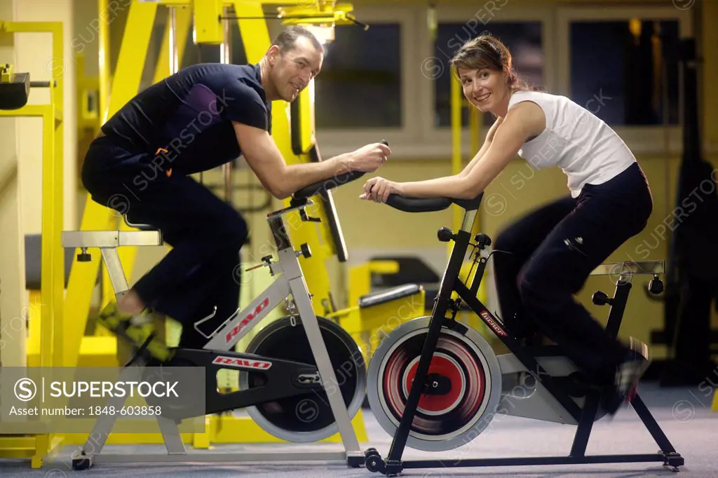 Couple sitting on exercise bikes, indoor cycling in a gym