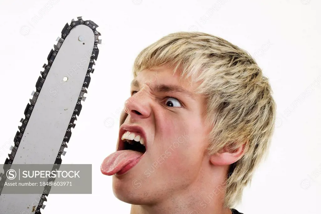 Young man with angry expression and outstretched tongue handling a chainsaw