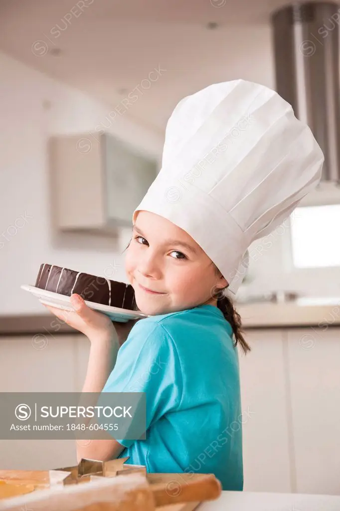 Girl in a chef's hat presenting a chocolate cake
