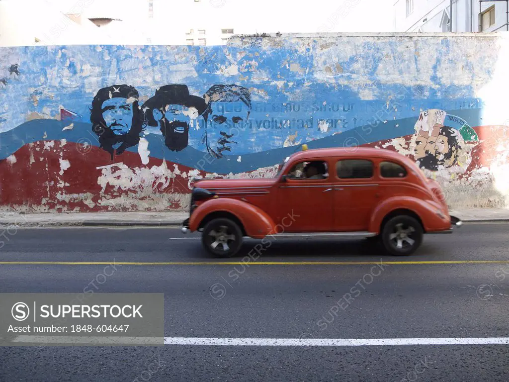 American vintage car driving along a wall with paintings of Fidel Castro and Che Guevara, Havana, Cuba, Latin America