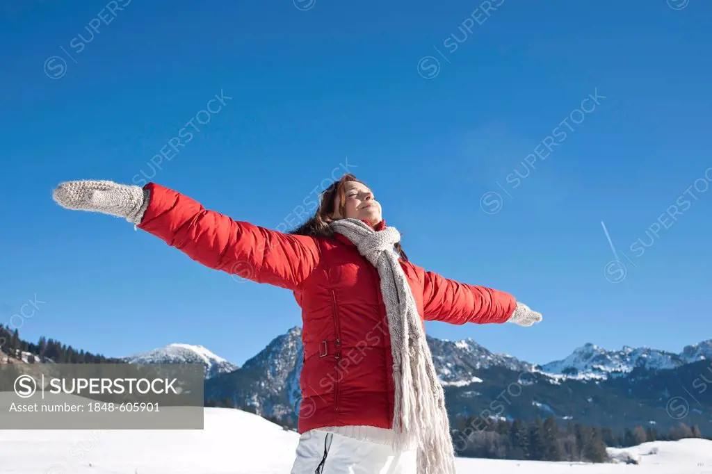 Woman standing in the snow with both arms raised sideways