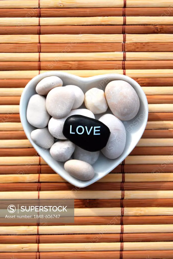 Hot stone massage stones, one labelled Love, in a heart-shaped porcelain bowl