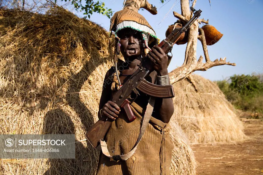 Woman of the Mursi ethnic group, famous for the huge lip plates the women are sporting, holding a rifle, Mago National Park, near Jinka, Lower Omo Val...
