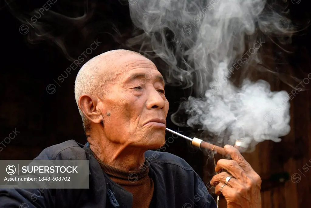 Male smoker, portrait, indulgence, old man of the Mouchi ethnic group smoking a pipe, smoke lingering in the air, Ban Mouchi Kaw village, Samphan dist...