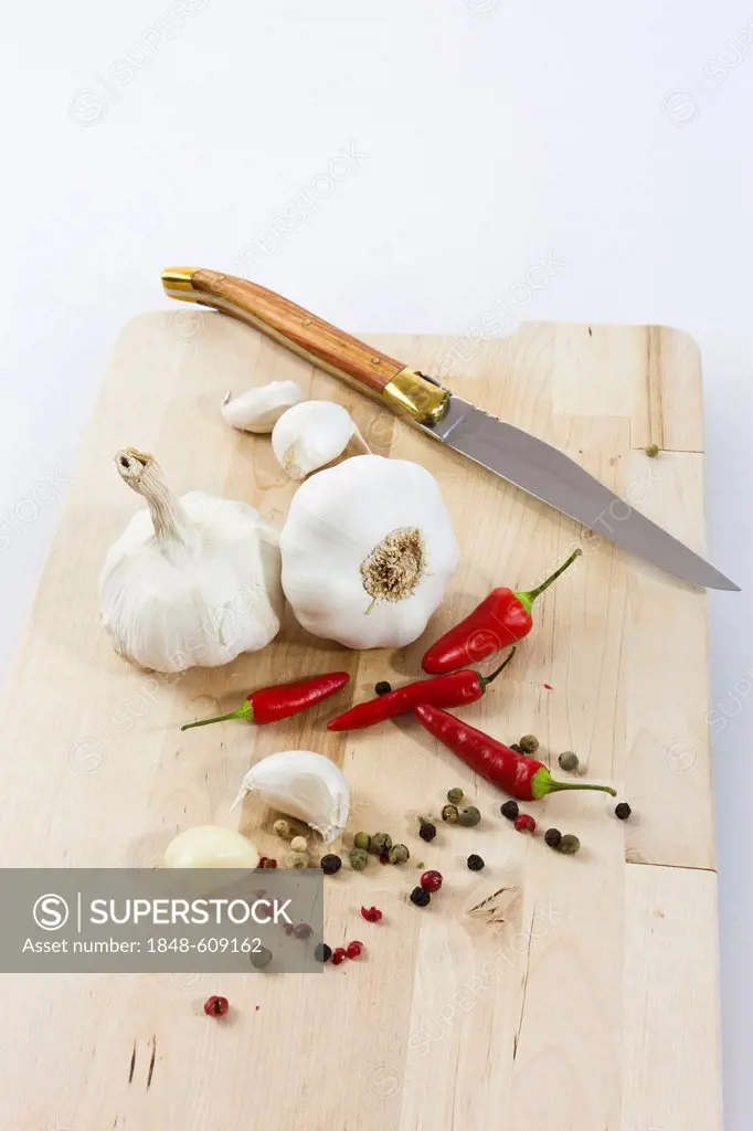Garlic (Allium sativum) on a wooden board with knife, chilis and black and red pepper