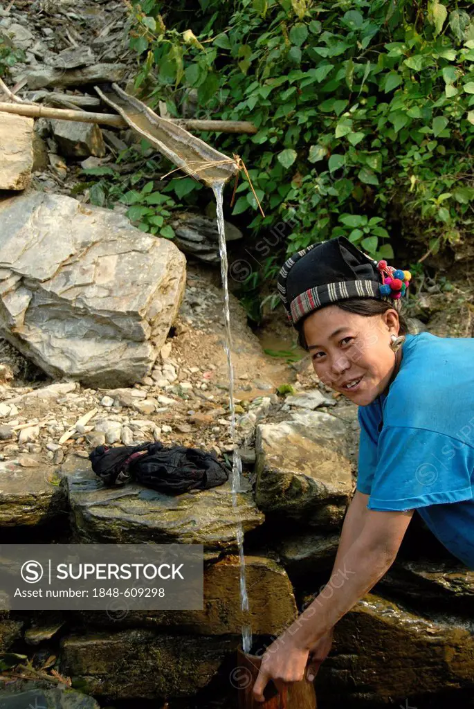 Drinking water from a spring, young woman of the Mouchi tribe drawing water with a bamboo vessel, traditional clothing, covered head with indigo-colou...