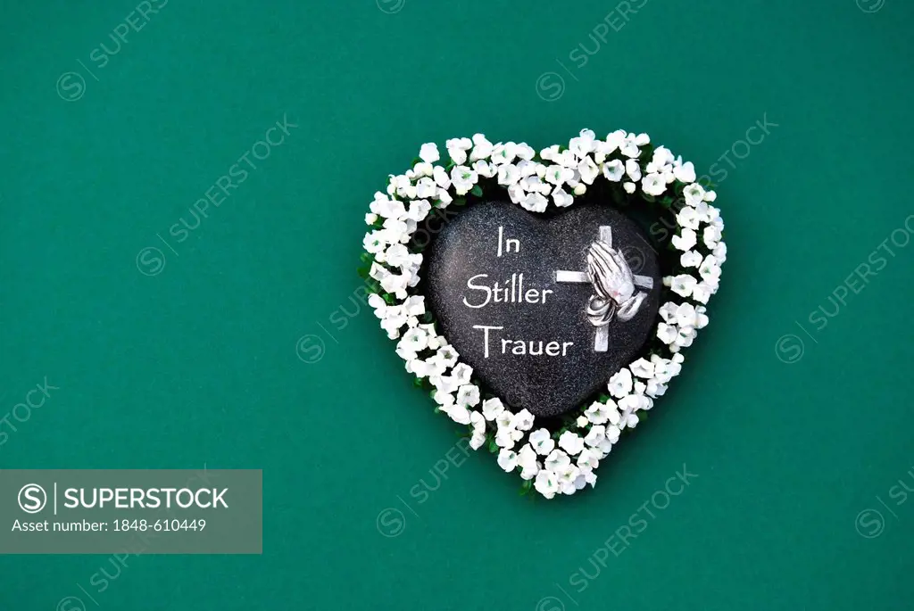 Heart of stone with the inscription In Stiller Trauer, German for In silent grief, heart-shaped stone framed with flowers, praying hands