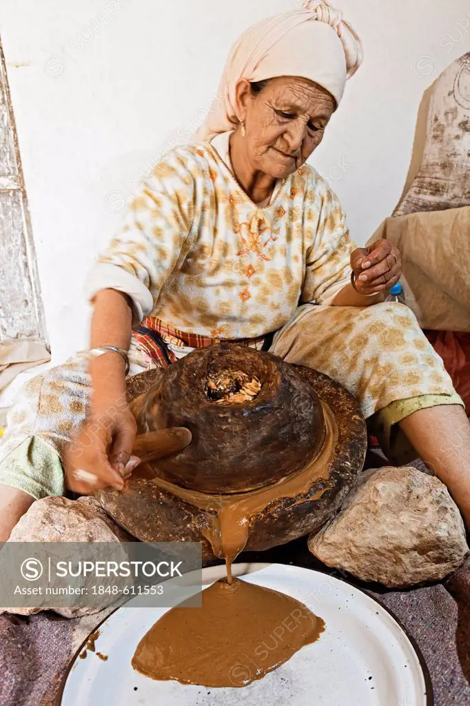 Woman grinding roasted Argan (Argania spinosa) almonds between two mill stones for the traditional manufacturing process of argan oil, near Essaouira,...