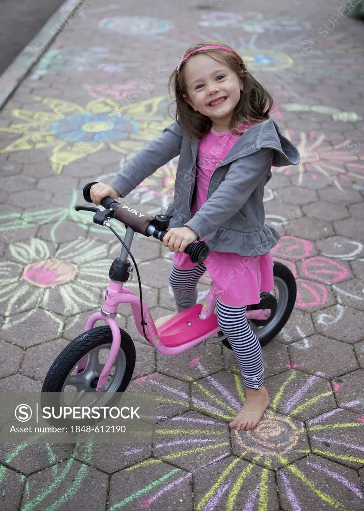 Three-year-old girl sitting on a walking bike, on a street painted with chalk, Rosenheim, Bavaria, Germany, Europe