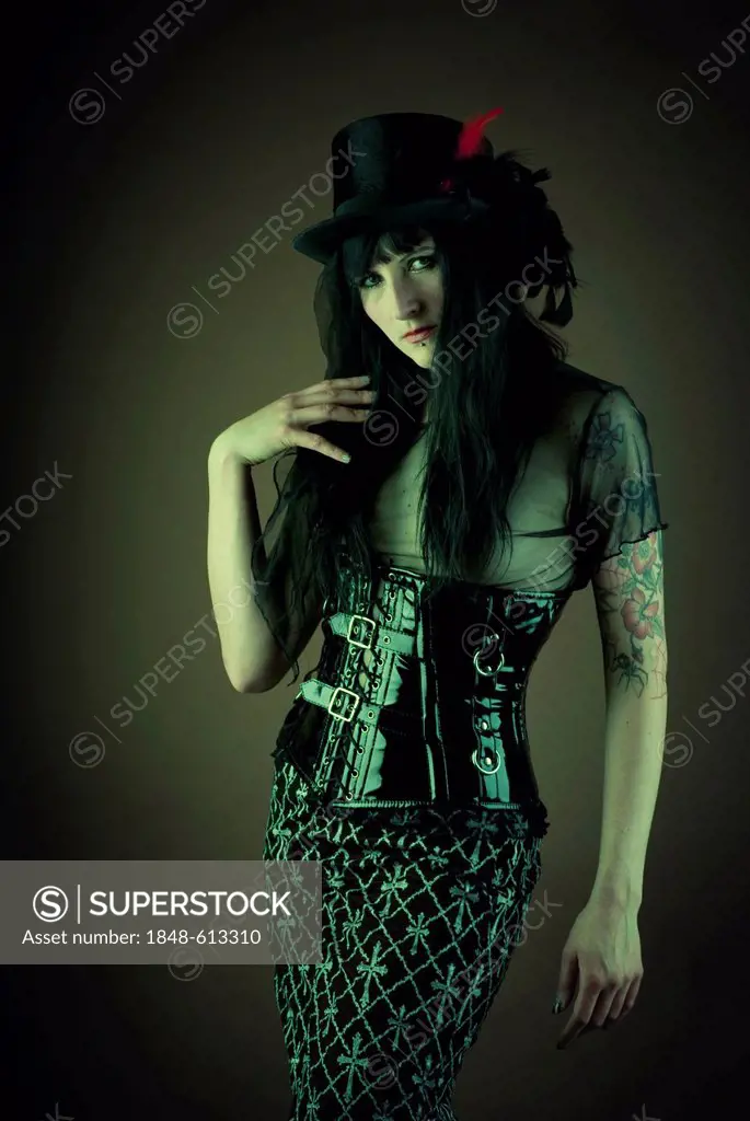 Woman, dressed in a Gothic style, wearing a latex corset and a hat, looking serious