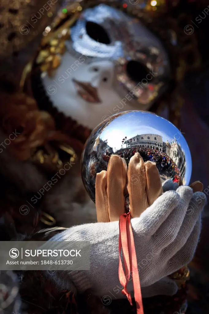 Woman dressed up for the Carnival in Venice holding a metal ball in which Piazza San Marco and people are reflected, Italy, Europe
