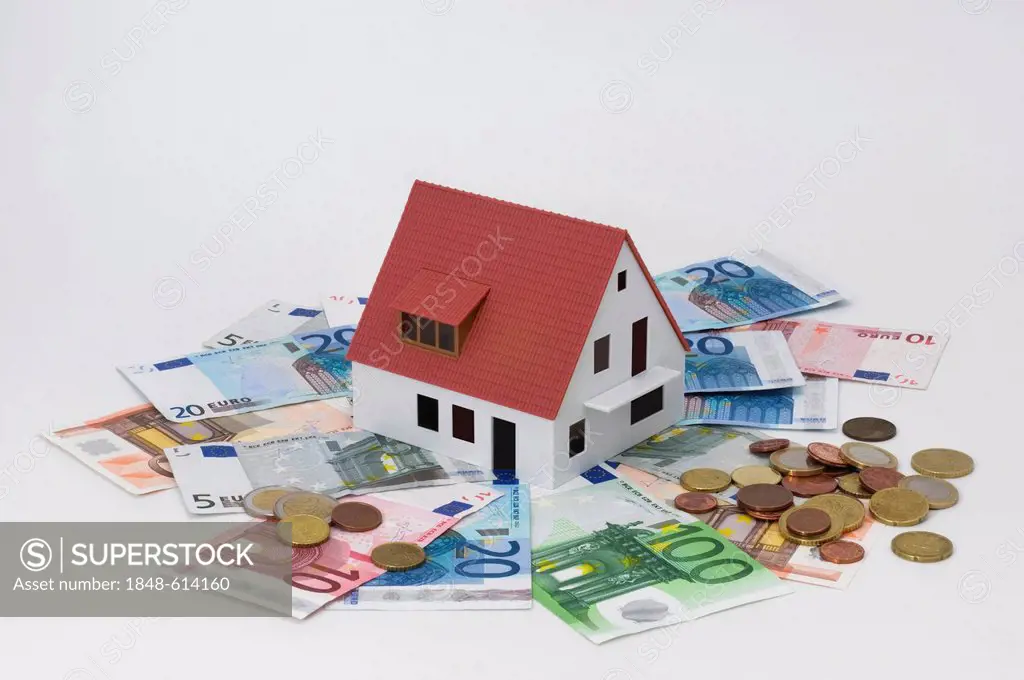 Miniature house surrounded by banknotes and coins, symbolic image for house building finance, investment or private property