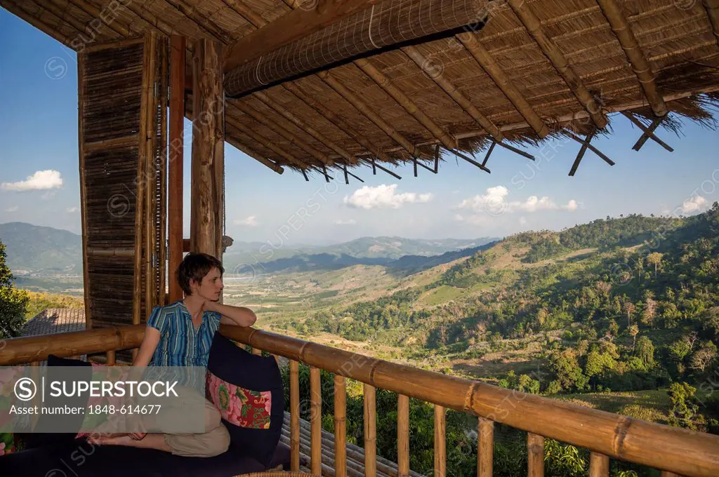 Woman sitting on a porch or veranda looking out into the landscape, bamboo hut, Lanjia Lodge, Northern Thailand, Thailand, Asia
