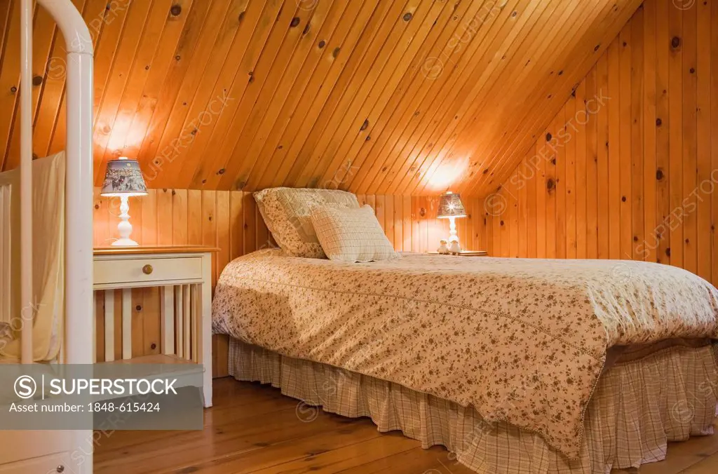 Bedroom with furnishings and knotty pinewood floor, walls and ceiling on the upstairs floor of a Canadiana cottage-style residential log home, Quebec,...